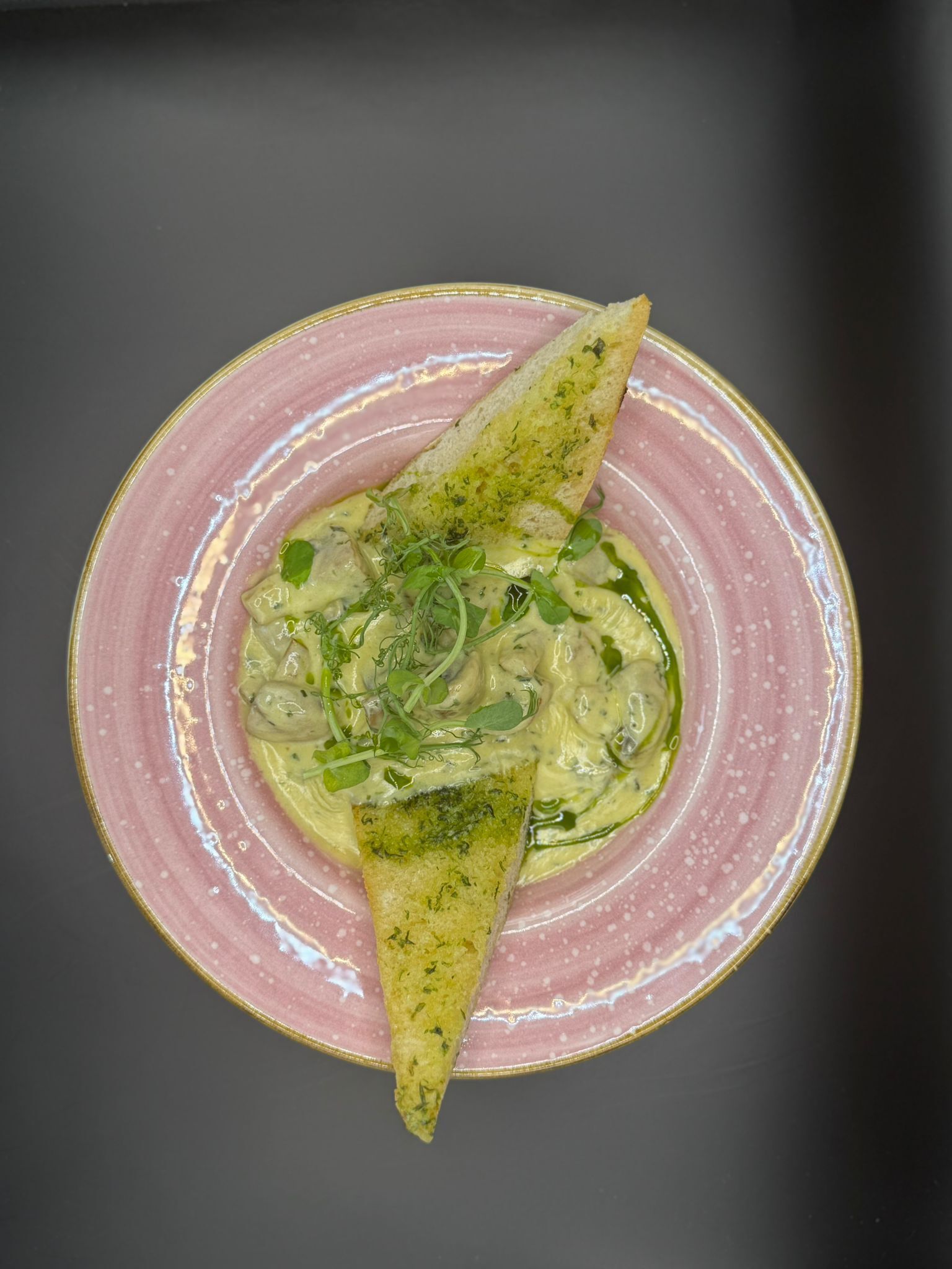 Un plato con un alimento, posiblemente una ensalada o una salsa, decorado con hierbas y un trozo de pan triangular.