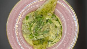 Un plato con un alimento, posiblemente una ensalada o una salsa, decorado con hierbas y un trozo de pan triangular.