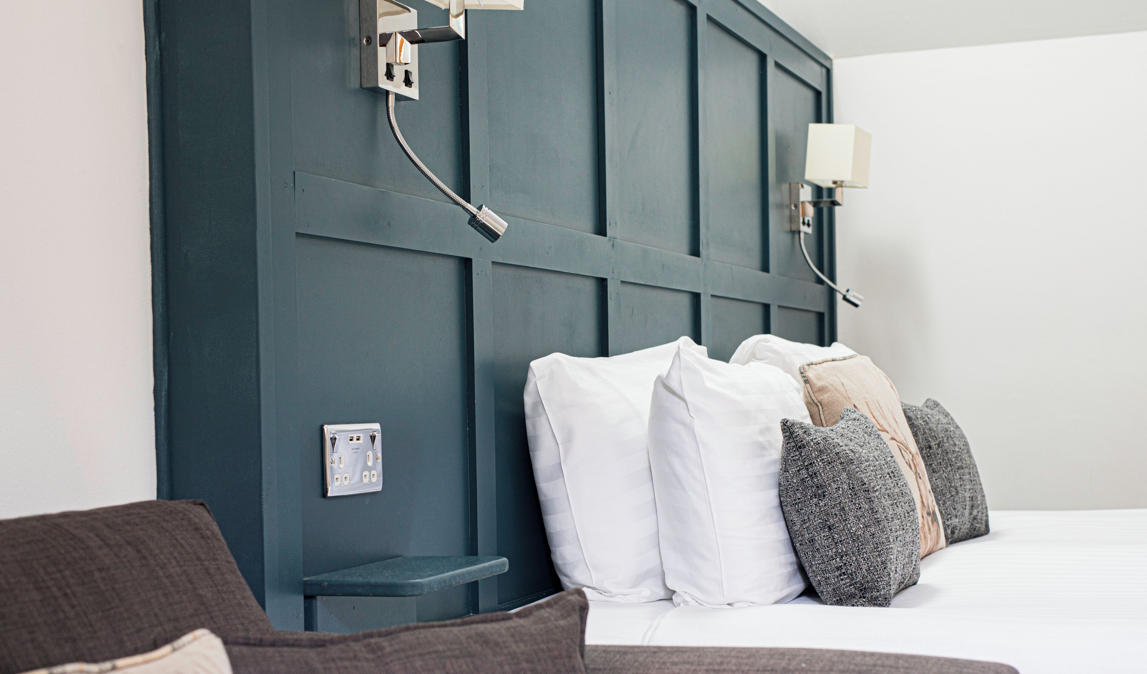 Un dormitorio con cabecera azul oscuro, cama blanca y lámpara de noche.