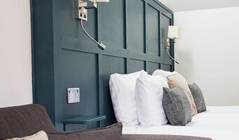 Un dormitorio con cabecera azul oscuro, cama blanca y lámpara de noche.