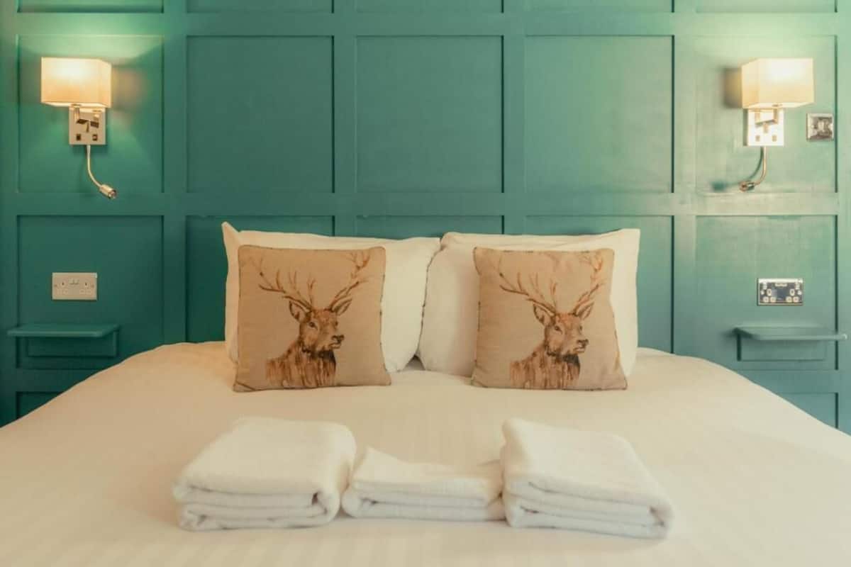 A bed with teal headboard, two wall-mounted lamps, and three pillows with deer designs.