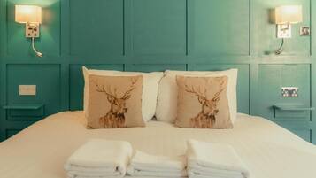 A bed with teal headboard, two wall-mounted lamps, and three pillows with deer designs.
