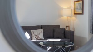 Un salon avec un canapé gris, une table basse en verre, une lampe et un tableau encadré au mur.