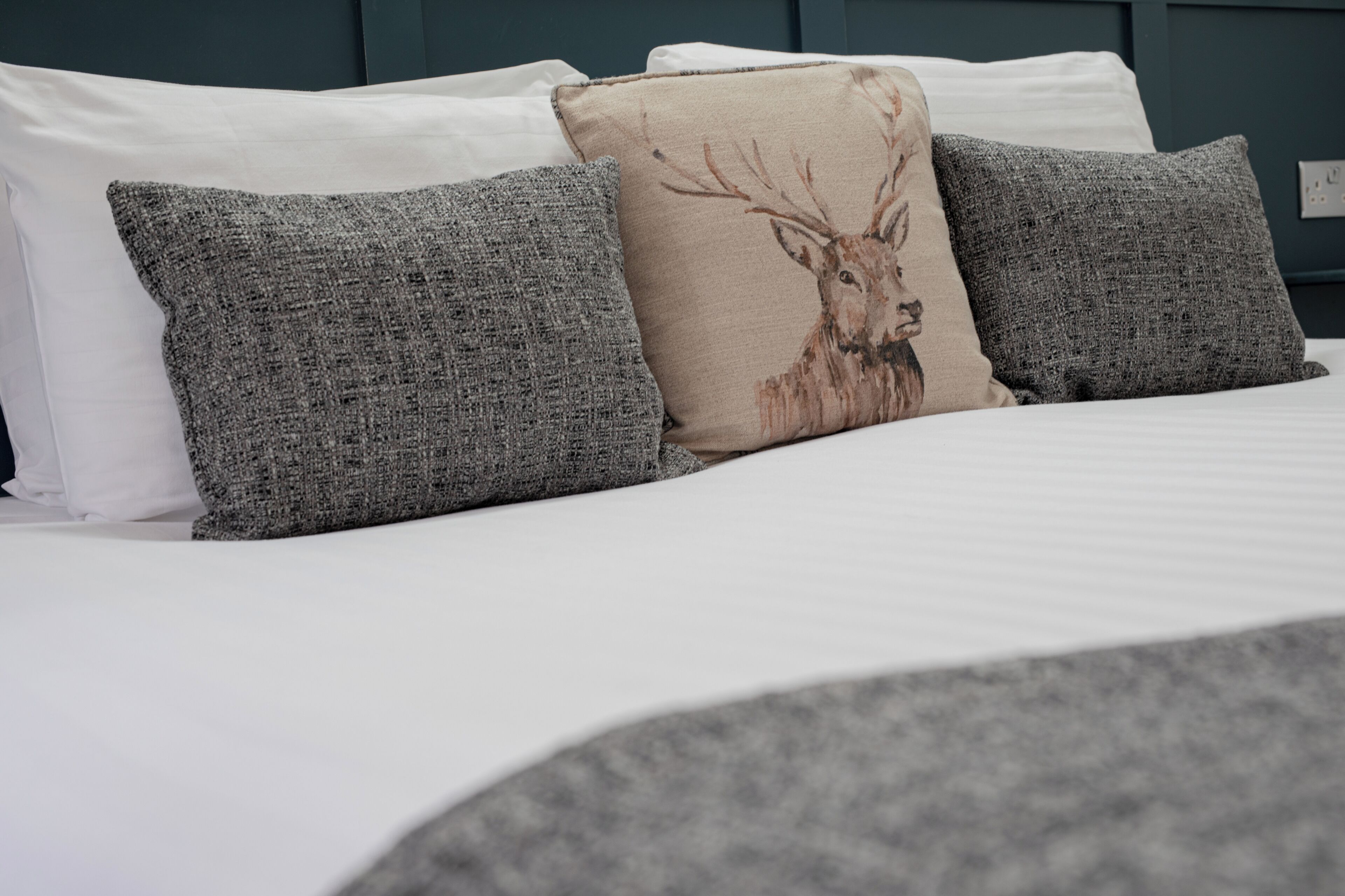 Un lit avec du linge de lit blanc et trois oreillers gris, dont un orné d’un motif représentant un cerf.