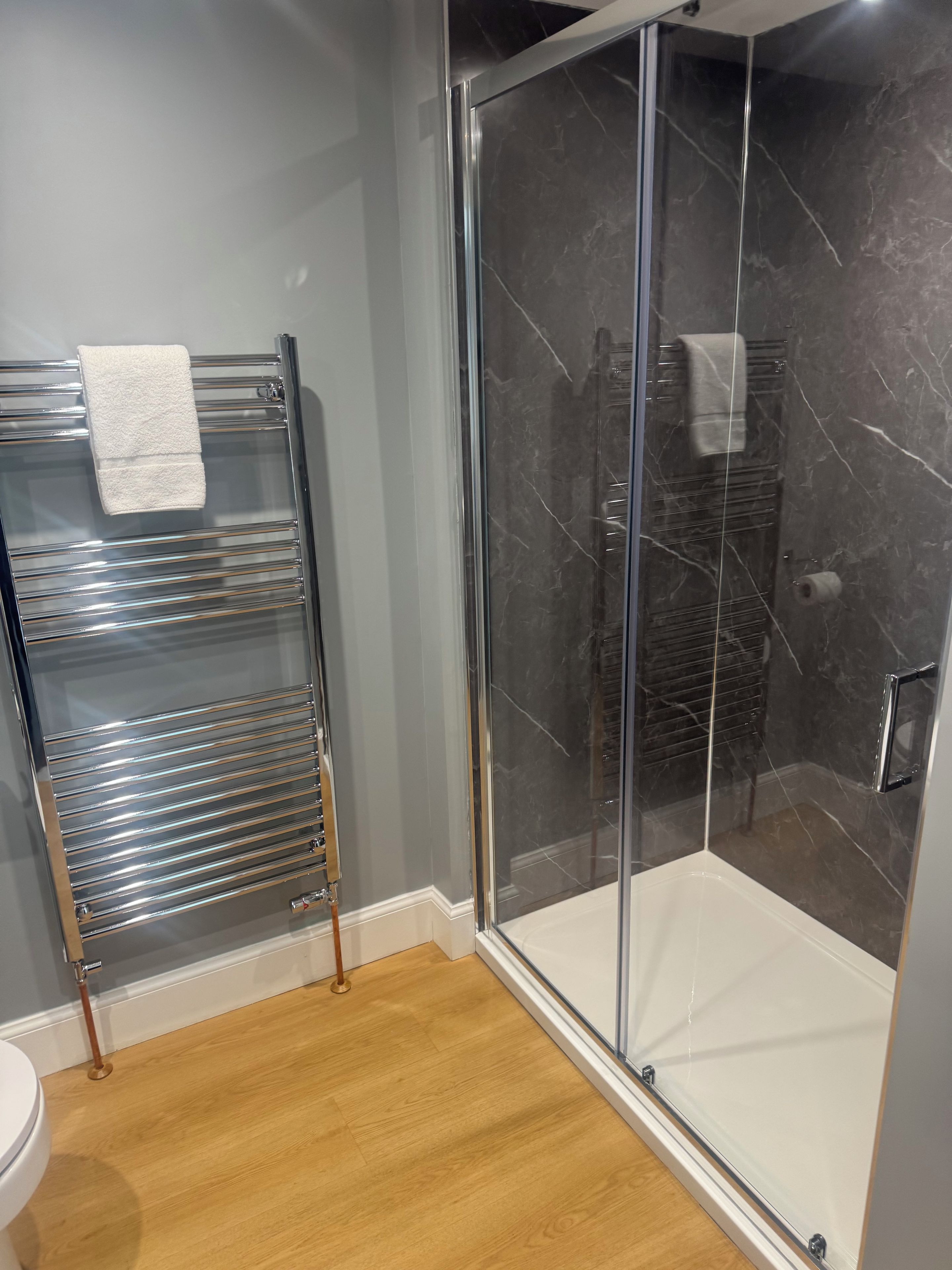 Un baño moderno con cabina de ducha de vidrio, un perchero cromado y suelo de madera.