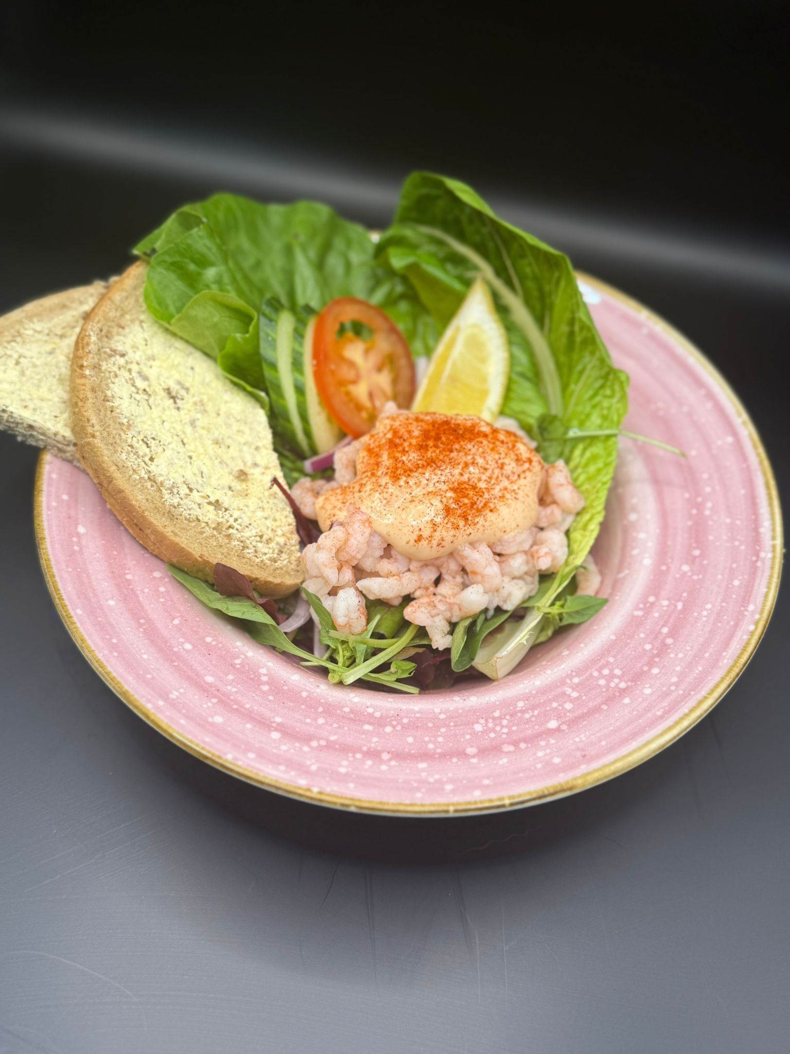 Un plato con un guiso de mariscos, una rebanada de pan y una rodaja de tomate sobre un plato rosa.