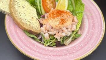Un plato con un guiso de mariscos, una rebanada de pan y una rodaja de tomate sobre un plato rosa.