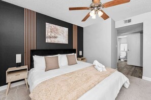 Un dormitorio moderno con una cama grande, un ventilador de techo, un panel de madera y un cuadro.