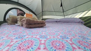 A tent with a bed inside, featuring a patterned bedspread and a stack of towels. - 212A-HOUSE TENT & GET 60-10 = 50 BIOBAY TOUR TEXT 787 614-5678 DATE-NAMES-EMAIL (Esperanza)