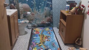 Ein Zimmer mit Fliesenboden, einer großen Wandmalerei von Meereslebewesen, einem Holzkabinett und verschiedenen Dekorationselementen.