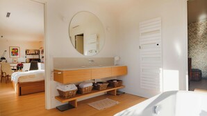 Ein modernes Schlafzimmer mit einem Holzbett, einem großen runden Spiegel, einer Holzkommode mit Waschbecken und Korbwannen.
