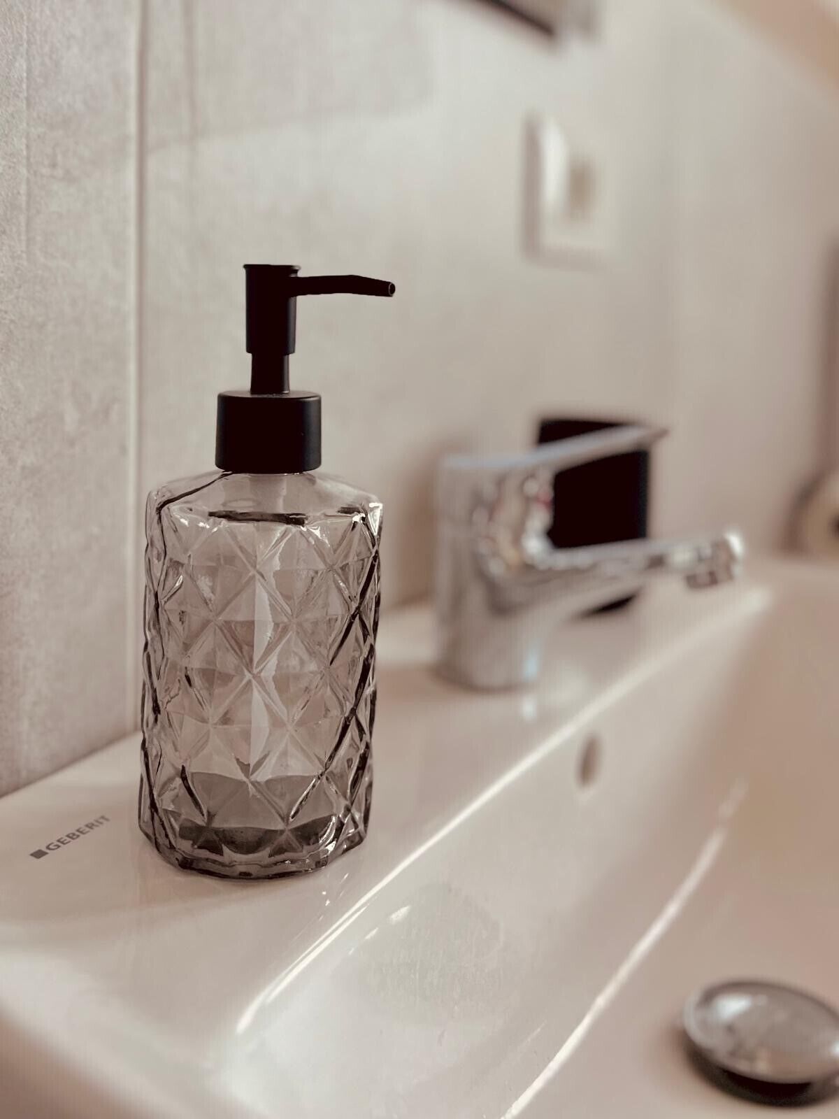 Un bagno con un flacone di vetro dotato di erogatore a pompa sul lavabo.