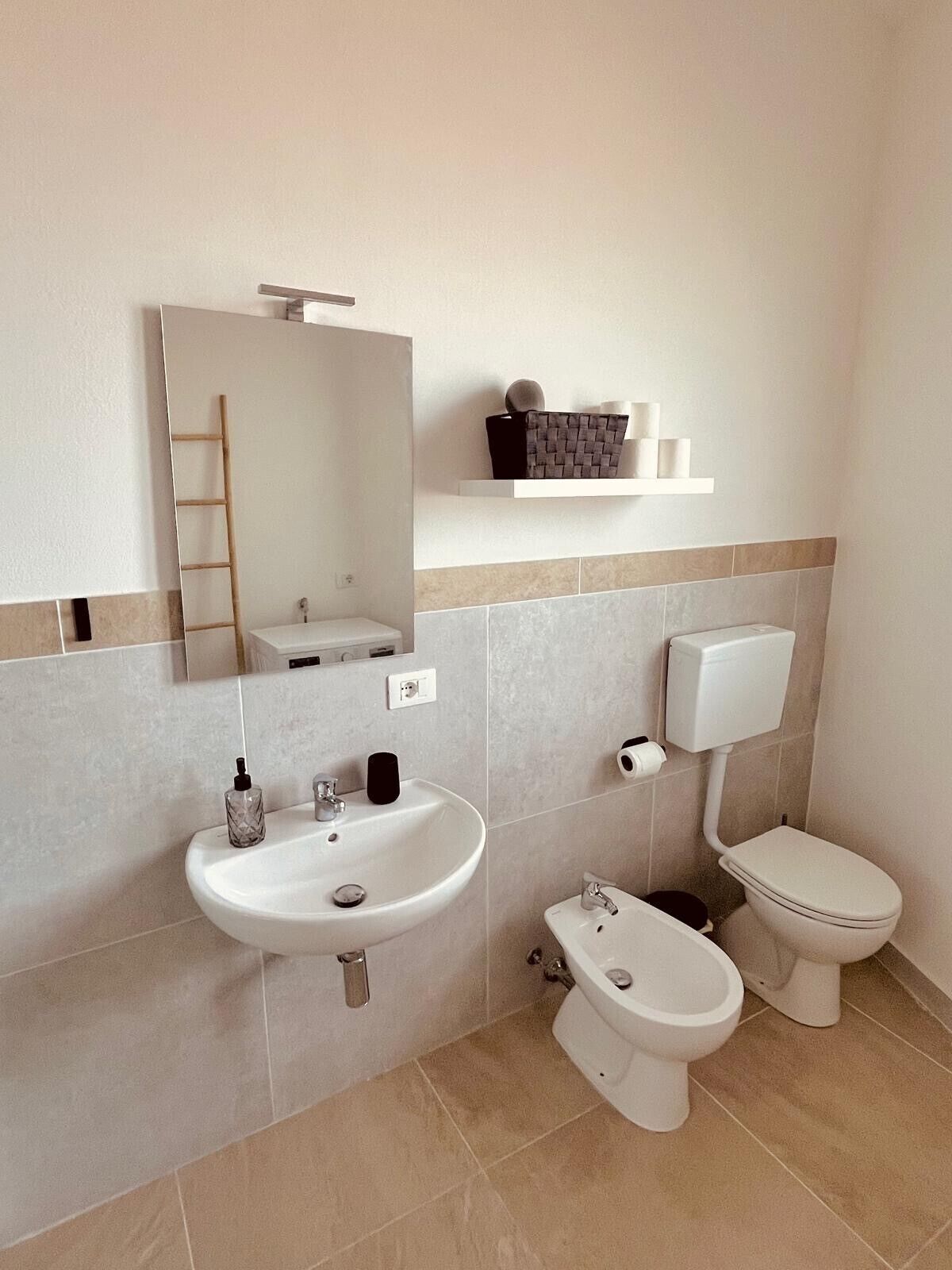 Une salle de bain moderne avec un lavabo blanc, un miroir, des toilettes et un bidet.