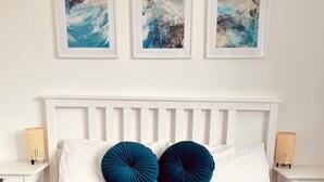 Uma cama com colcha azul acolchoada, duas almofadas azul-escuras, cabeceira branca e duas mesas de cabeceira com abajures.