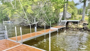 A wooden dock extending over a body of water, surrounded by trees and a small house with a deck. - WATERFRONT ON BRANDY POND!  SLEEPS 20!! (Naples)