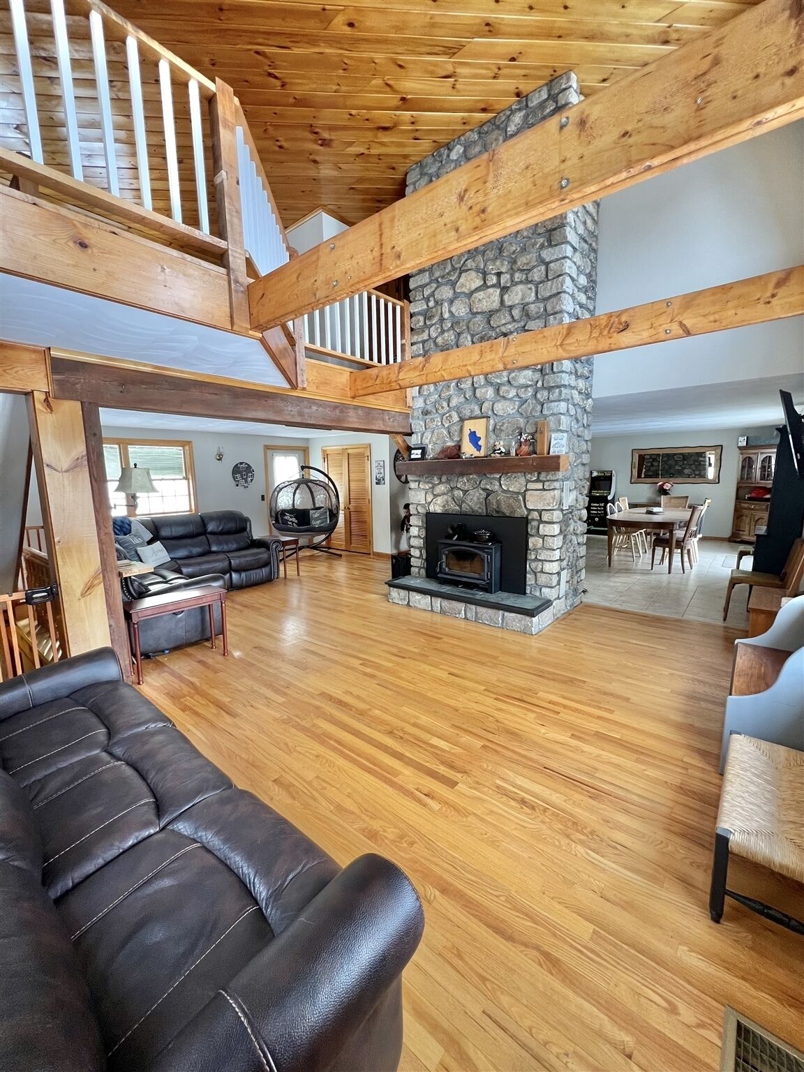 A spacious living area with a stone fireplace, wooden beams, and a high ceiling.