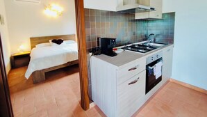 A compact hotel room with a kitchenette, a bed with white bedding, and a small bedside table. - Garin Knoll (Bolsena)