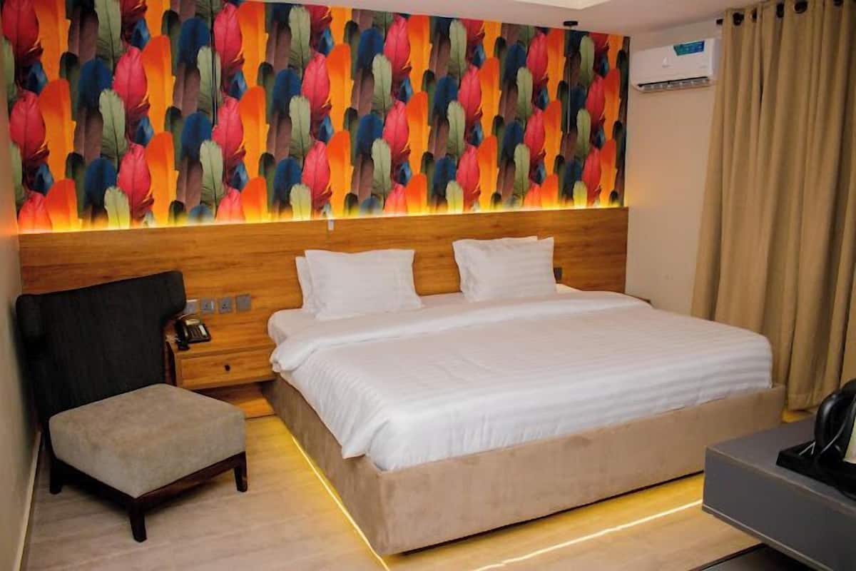 Une chambre d’hôtel avec un grand lit, un petit coin salon, une table de chevet et une fresque murale aux couleurs vives.
