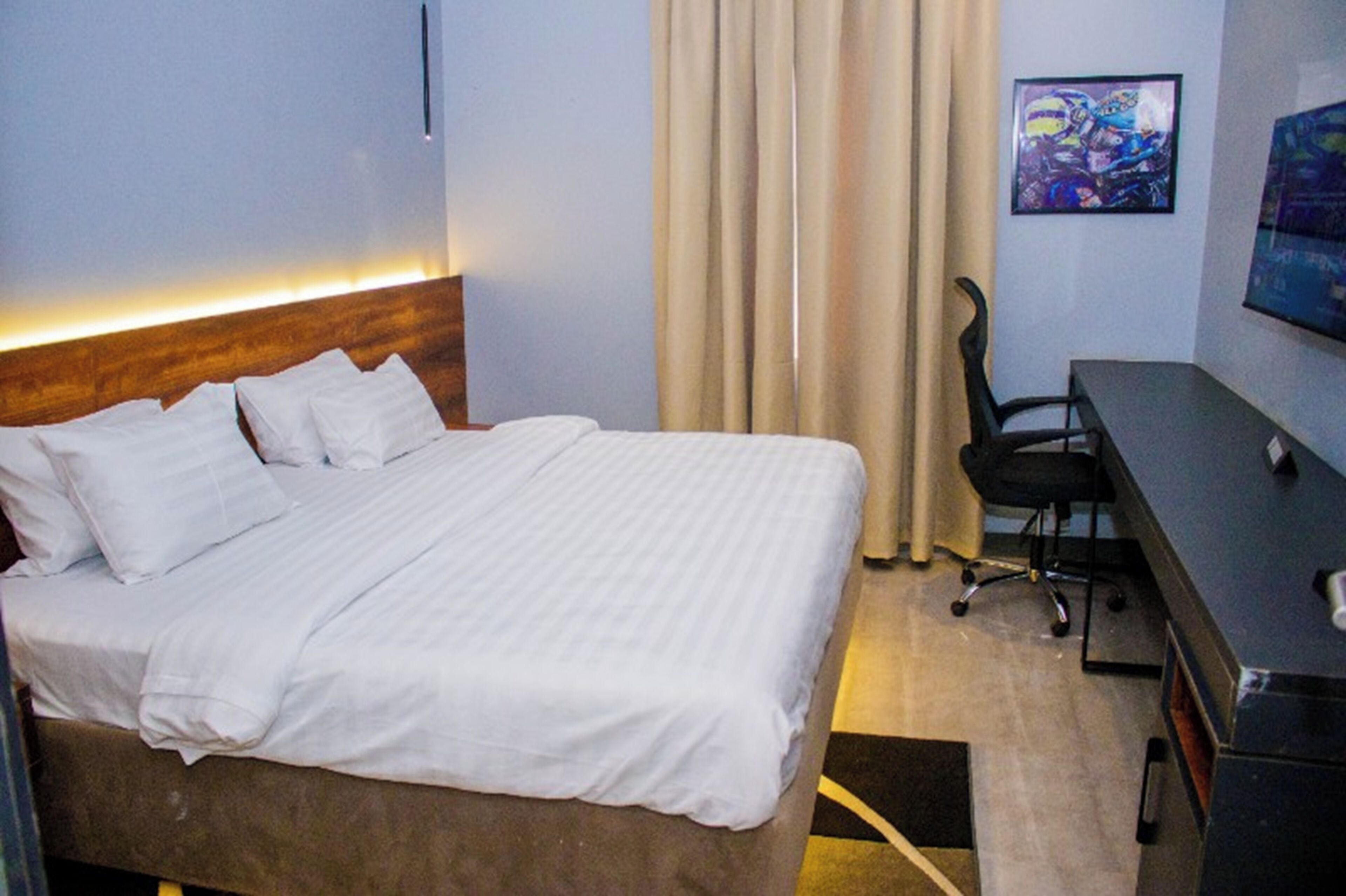 A hotel room with a bed, a desk, a chair, a TV, and a curtain.