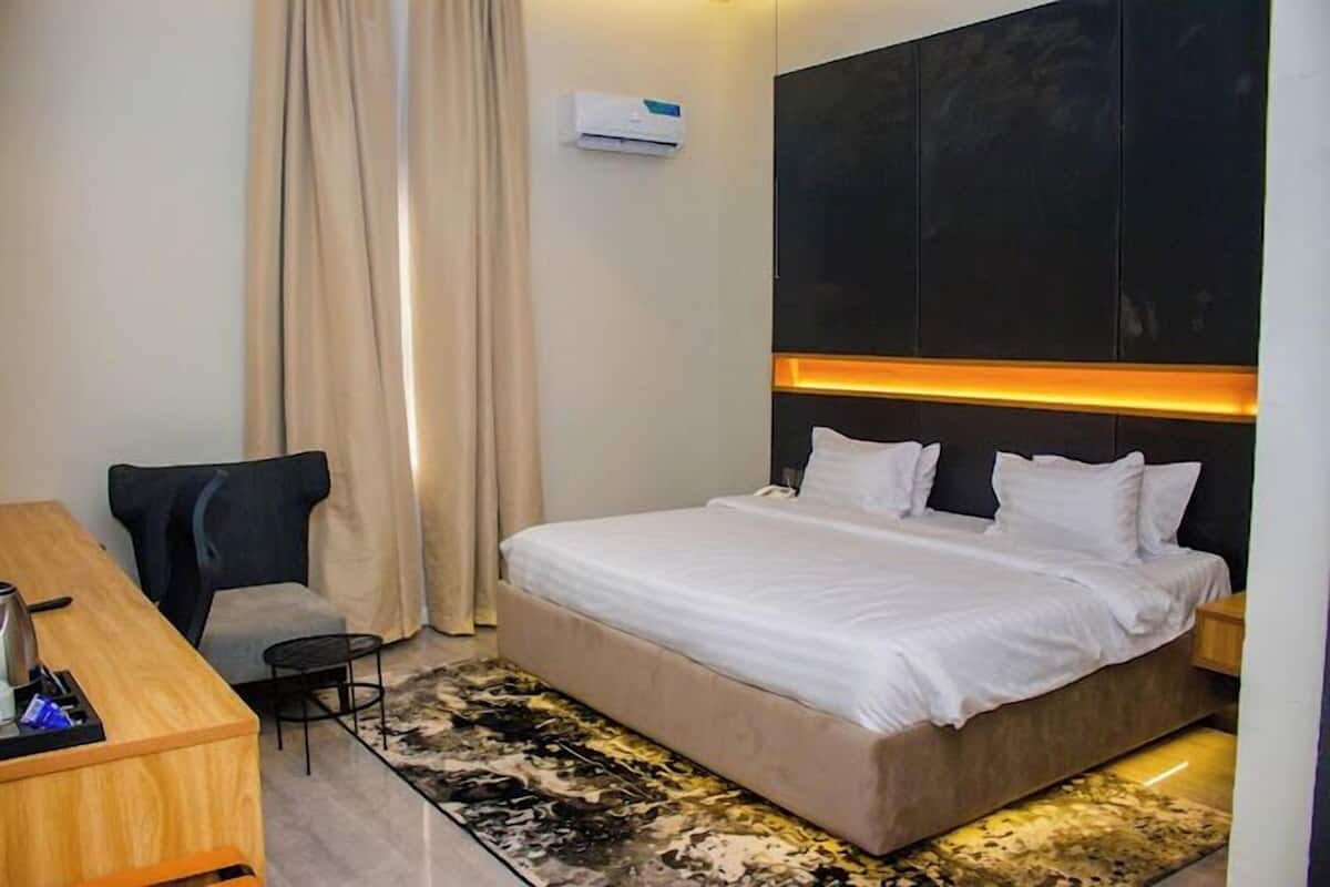 Une chambre d’hôtel équipée d’un lit, d’un bureau, d’une chaise, d’un climatiseur et d’un tapis à motifs.