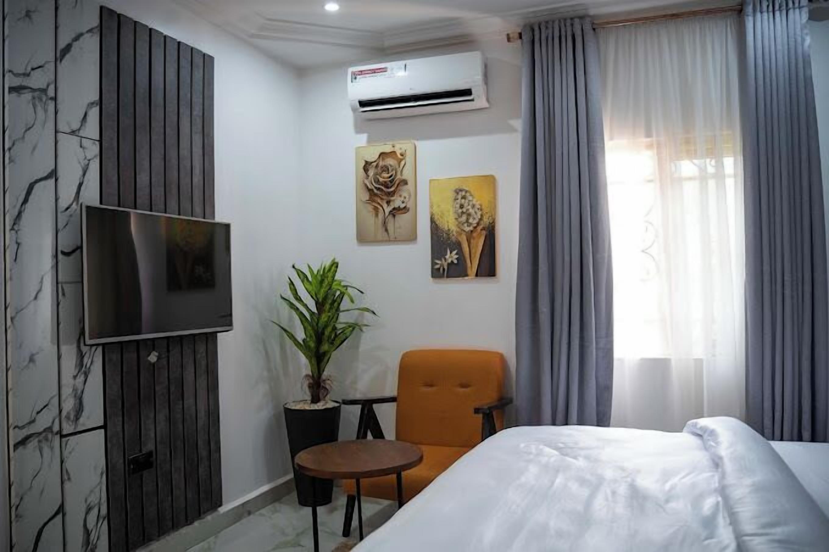 A hotel room with a bed, a TV, a potted plant, and artwork on the wall.