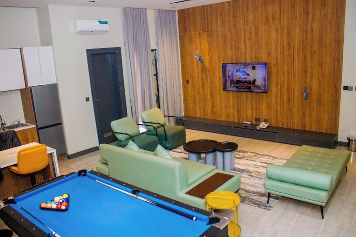 Une table de billard, des canapés verts, un téléviseur et un mur en bois.