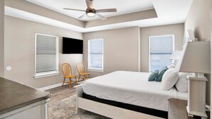 A bedroom with a bed, two chairs, a desk, a ceiling fan, and two windows with blinds. - Gulf Front Duplex | Shared Pool | West Beach (Gulf Shores)
