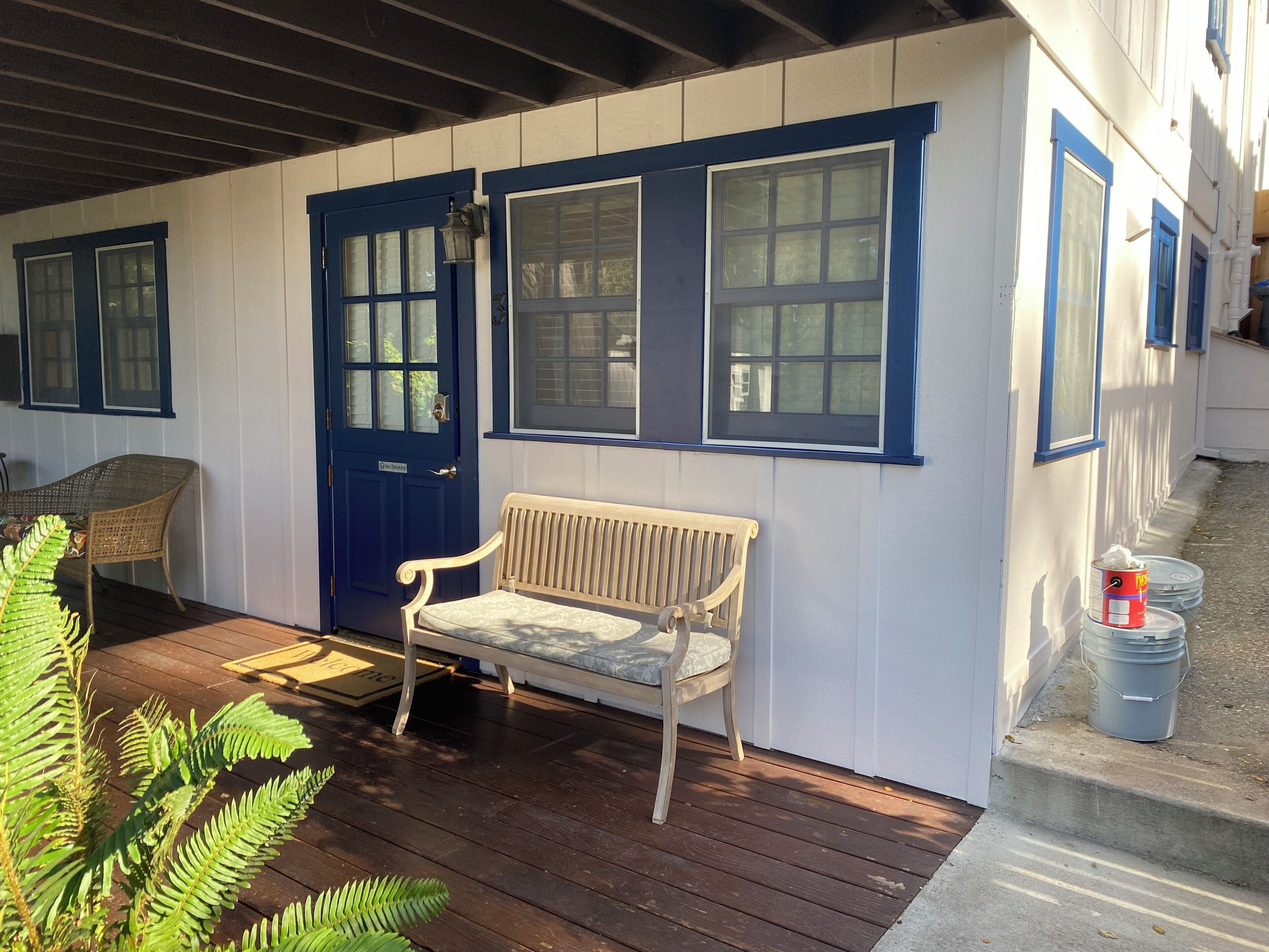 A porch with a bench, a blue door, and windows with blue trim.