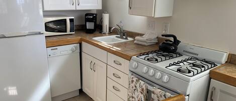 Cocina compacta con alacenas blancas, microondas, cafetera, estufa a gas y lavavajillas.