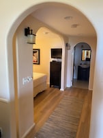 A hallway with a bed, a TV, a dresser, and a bathroom visible through an archway.