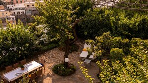 A rooftop pool area with a stone deck, surrounded by lush greenery and overlooking a hillside town with colorful buildings. - Villa Maelle by My Villa Collection (Positano)