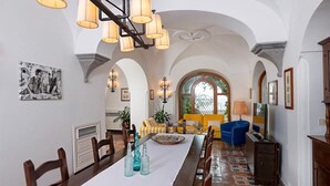 A spacious dining area with a long table, chairs, and a chandelier. There are two sofas and a TV stand. - Villa Maelle by My Villa Collection (Positano)