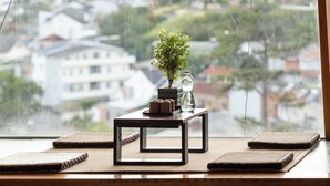 A view through a window with a table holding a plant, a vase, and a tray of pastries. - Pha Boutique House (Xuan Huong - Da Lat)