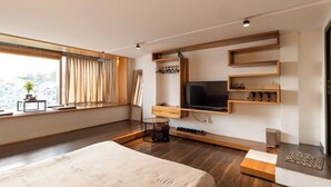 A modern bedroom with a large bed, a TV mounted on a wooden shelf, a window with curtains, and a city view. - Pha Boutique House (Xuan Huong - Da Lat)