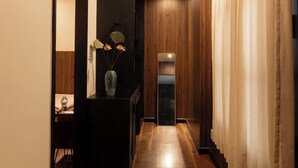 A hallway with wooden flooring, a dark console table with a vase and flowers, a mirror, and a staircase with curtains. - Pha Boutique House (Xuan Huong - Da Lat)