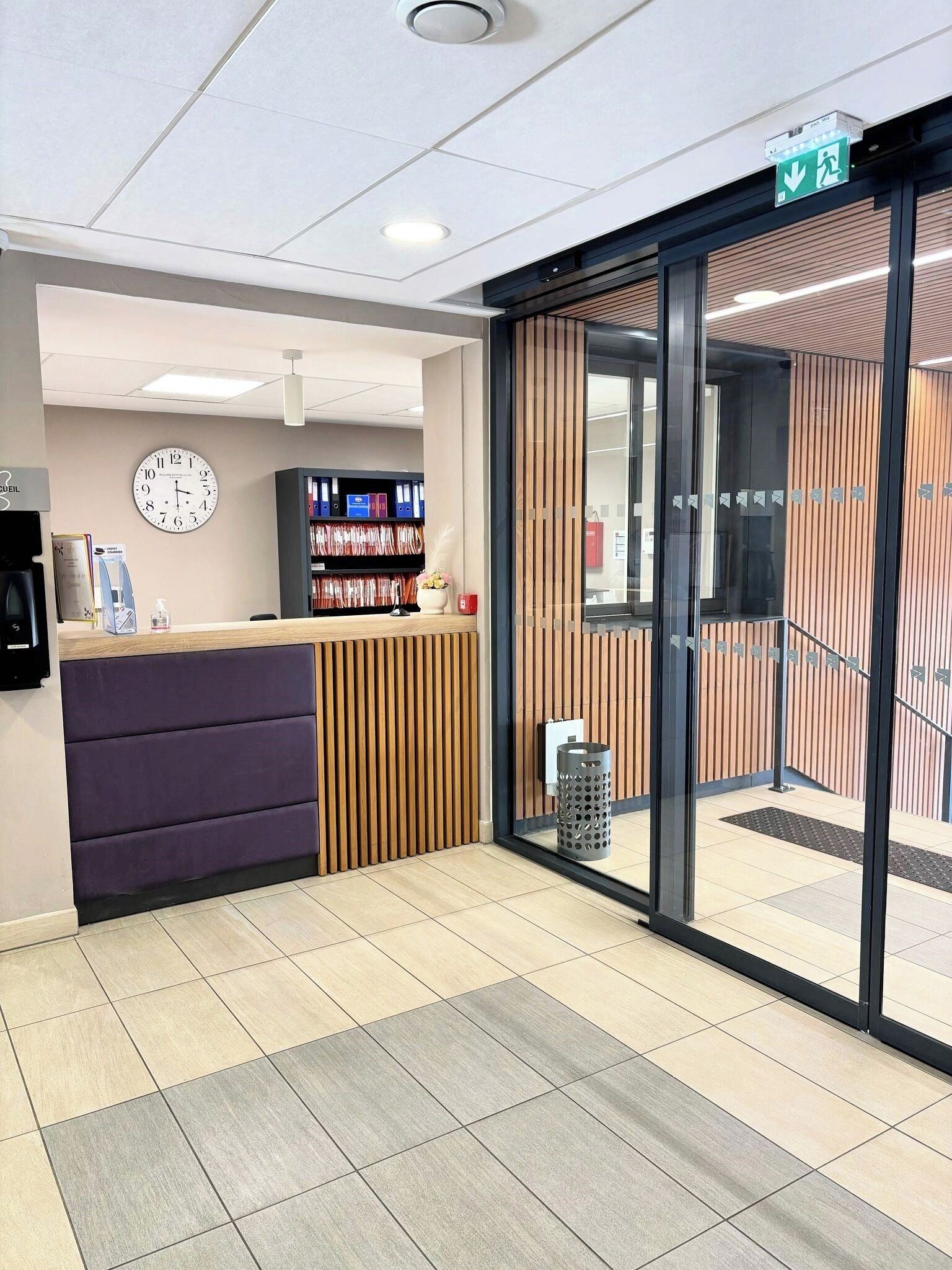 A reception area with a reception desk, a clock, and a wall-mounted shelf with binders.