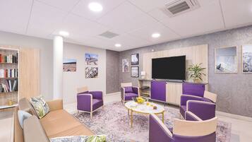 Een moderne woonkamer met een bank, paarse fauteuils, een salontafel en een boekenkast.