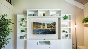 Een moderne woonkamer met een flatscreen televisie, bevestigd aan een witte tv-meubel, omringd door planken met planten en decoratieve objecten.