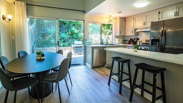 Een moderne keuken met een centraal eiland, barstoelen en een eettafel met stoelen.