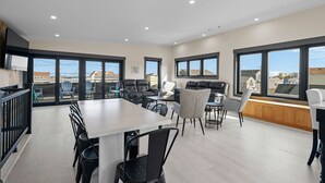 A spacious room with a large dining table, multiple chairs, and a view of the city through large windows. - Easy Beach Access, Sleeps 12 (Old Orchard Beach)