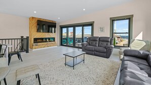 A spacious living room with a fireplace, leather sofa, and large windows offering a view of the outside. - Easy Beach Access, Sleeps 12 (Old Orchard Beach)