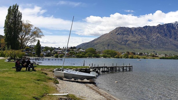 A lakeside view with a dock, a sailboat, and a mountain in the background.