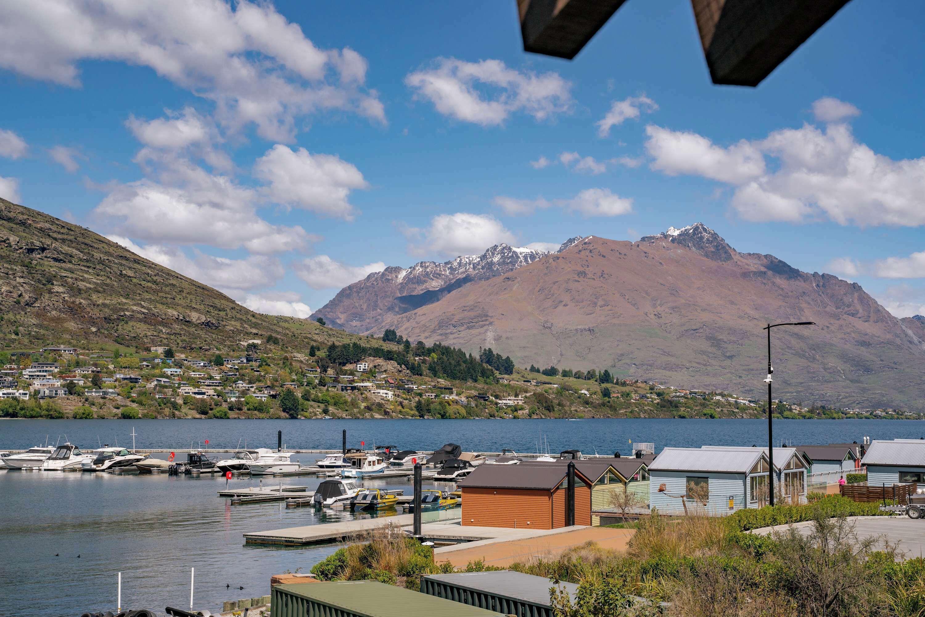A marina with boats docked, a small wooden building, and a mountain in the background.