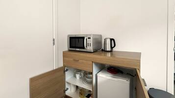 A compact kitchenette with a microwave, kettle, and refrigerator.