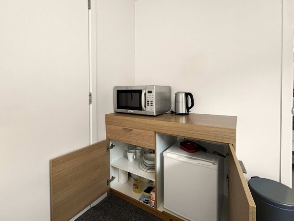 Una kitchenette compacta equipada con microondas, tetera y refrigerador.