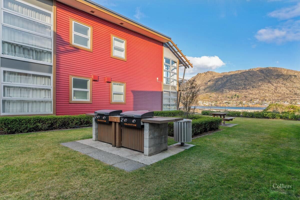 A red building with a barbecue area, a trash bin, and a bench.