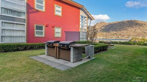 A red building with a barbecue area, a trash bin, and a bench.
