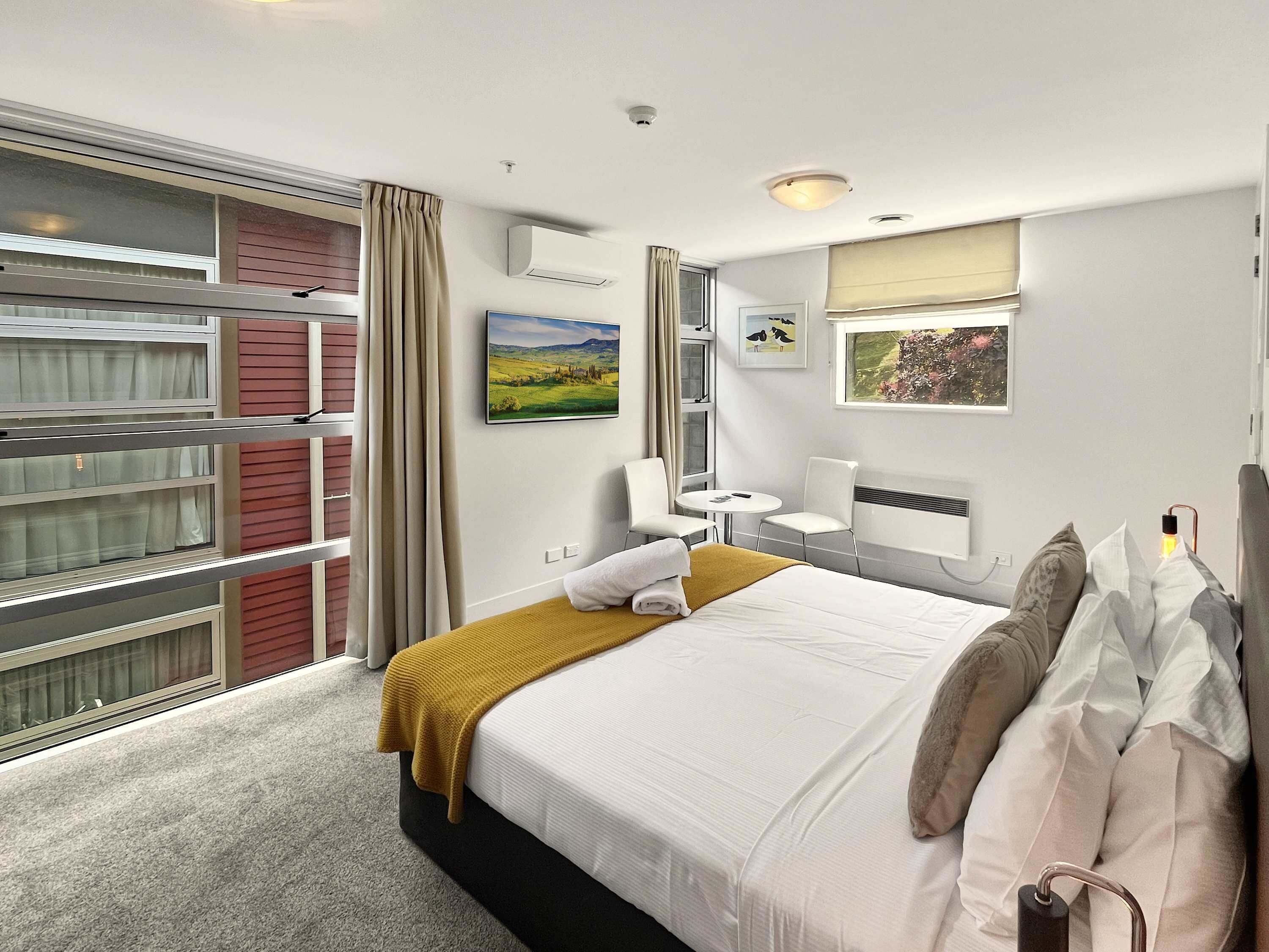 Een hotelkamer met een bed, een tafeltje, stoelen, een raam met gordijnen en kunstwerken aan de muur.