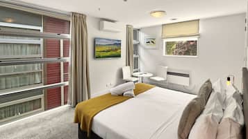 A hotel room with a bed, a small table, chairs, a window with curtains, and artwork on the walls.