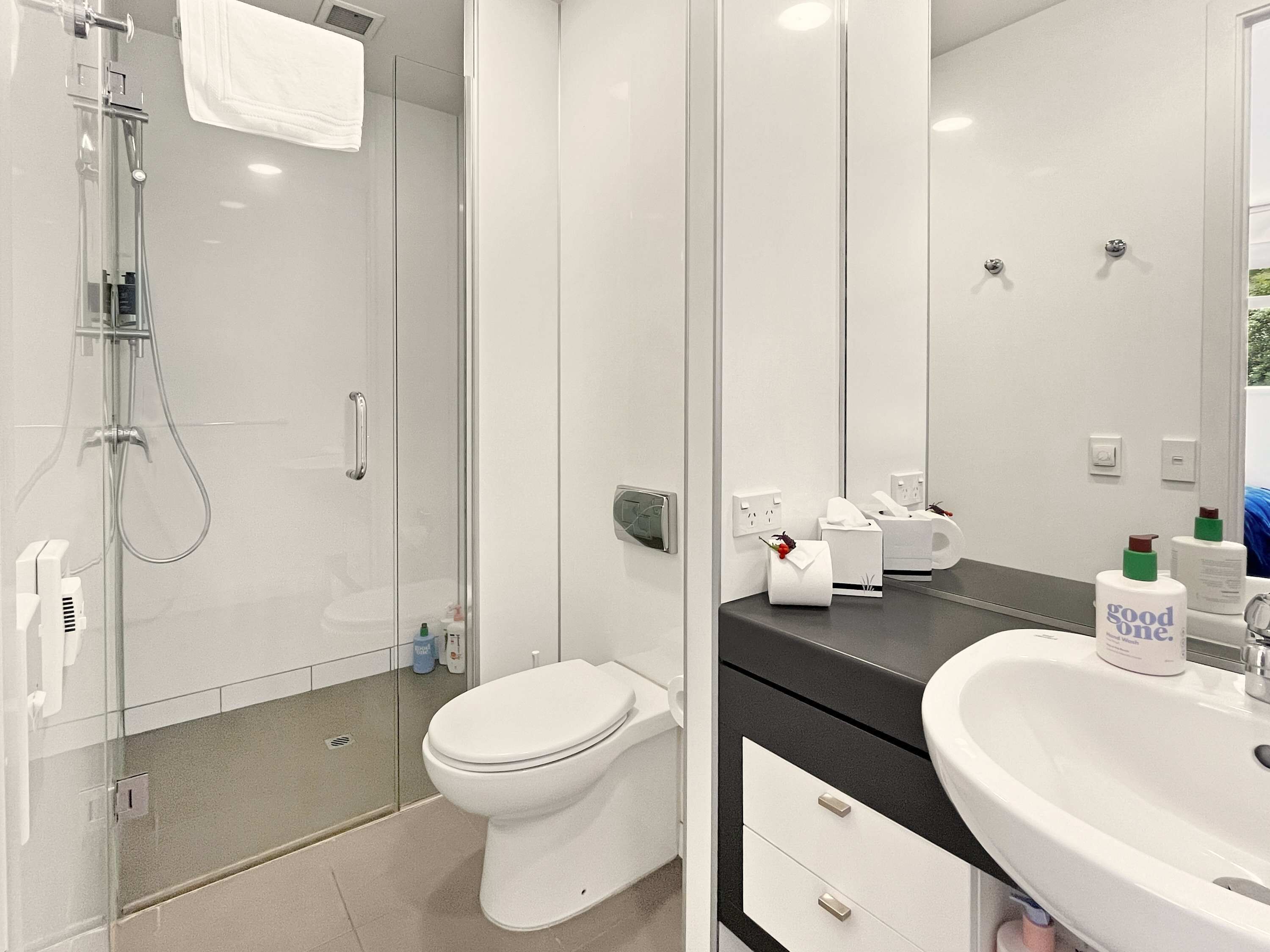 A modern bathroom with a glass shower enclosure, a toilet, a sink with a mirror, and toiletries on the counter.